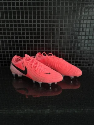 Nike Phantom elite rosa fotbollsskor - Säljer ett par Nike Phantom elite fotbollsskor i en riktigt snygg rosa färg med svarta detaljer och klassisk Nike-logga. Skorna har dobbar för spel på gräs och är tillverkade i syntetmaterial med snörning för bra passform. Perfekta för dig som vill sticka ut på planen!