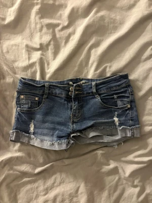 Blå denimshorts med slitningar - Snygga blå jeansshorts i klassisk denim med slitna detaljer och upprullade benslut.