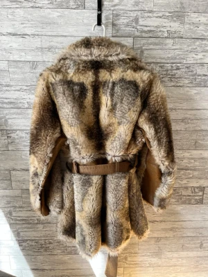 Brun och beige pälsjacka med bälte - Säljer en fluffig pälsjacka i bruna och beige toner med bred krage och stora fickor framtill. Jackan har ett matchande bälte i midjan och stängs med knappar.