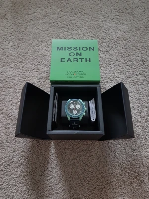 Omega x Swatch Mission on Earth klocka - Säljer en Omega x Swatch Speedmaster MoonSwatch Mission on Earth. Klockan har en mintgrön boett i biokeramik, svart urtavla med vita subdials och blå bezel. Svart textilband med Omega-logga. En riktigt unik och cool accessoar för dig som gillar statement pieces.