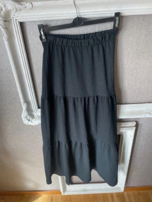 Svart långkjol med volangdetaljer - En svart långkjol med volangdetaljer och resår i midjan. Kjolen har en luftig och flowy passform