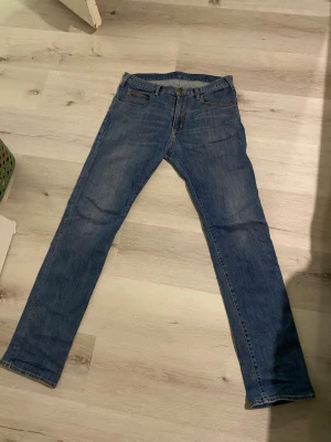 Blå jeans från Armani - Säljer ett par klassiska blå slim fit jeans från Lee. Jeansen har fem fickor, normal midja och raka ben. Tillverkade i slitstark denim med snygg tvätt och Armani bak i midjan. Perfekta för en avslappnad och stilren look.