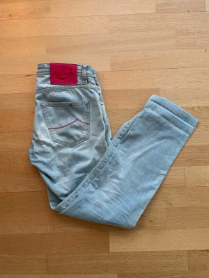 Jacob Cohën Slim Fit Jeans - Jacob Cohën slim fit jeans i ljusblå. Mycket bra skick, använda ett fåtal gånger och har ett mycket bra helhetsintryck. Mått: 39 cm midja, 96 cm längd. Material: 98% bomull, 2% elastan. Säljes som de är. Skickas välpackade inom 24 timmar.