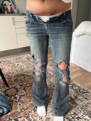 Blå slitna bootcut jeans - Säljer ett par blå bootcut jeans med kraftiga slitningar och hål på båda benen. Materialet är denim i bomull. Har haft hål mellan benen men det har lagats ordentligt hos en skräddare så kommet definitivt inte bli hål där igen 👍
