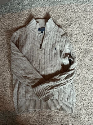 Grå kabelstickad tröja Polo Ralph Lauren - Snygg grå kabelstickad tröja från Polo Ralph Lauren med halv dragkedja - storlek för 14/15 åringar - använd ett fåtal gånger - skriv om ni är intresserade!