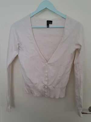 Ljusrosa kofta - Ljusrosakofta från H&M med djup v-ringning och långa ärmar. Koftan har ribbade muddar och knäpps med vita knappar framtill. Färgen är väldigt väldigt ljusrosa. Str. 38