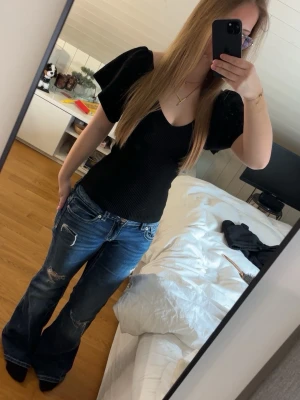 Svart ribbad topp från Only - Fin svart ribbad topp med puffiga korta ärmar och v-ringning. Toppen har en söt knytning i nacken. Materialet är skönt och strechigt, och formar sig efter sin kropp. Väldigt skön topp men är tyvärr inte längre min stil och kommer aldrig till användning.