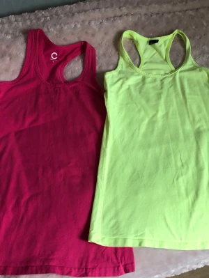 Två linnen i neon och cerise - Två snygga linnetoppar, en i neon-gul och en i cerise. Båda har brottarrygg och är tillverkade i mjuk bomull, perfekta för en avslappnad och sportig stil.  Längd: 72cm. Armhåla till armhåla: 40cm. 50kr för båda.