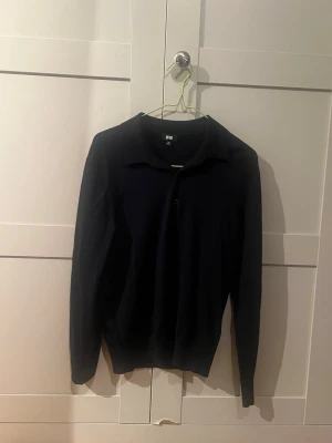 Svart långärmad tröja från Uniqlo - En stilren svart långärmad tröja från Uniqlo med klassisk krage och enkel knäppning framtill. Perfekt för dig som gillar minimalistisk design och mjuka material. Passar till många olika outfits och är lätt att matcha.