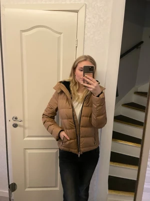 Vero Moda ljusbrun pufferjacka med skön huva - Säljer en ljusbrun pufferjacka med huva och dragkedja framtill. Jackan har en quiltad design och är vadderad för extra värme. Fejk päls i huvan, super skön. Håller värmen jättebra. Har älskat denna. Så bekväm och stilren. Perfekt för kalla vinterdagar och har en enkel, stilren look som passar till det mesta. Mycket gott skick. Börjar tyvärr bli för liten. 