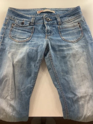 Ljusblå jeans från Only - Säljer ett par ljusblå jeans från Only med snygg slitning och utsvängda ben. Jeansen har klassiska fem fickor, låg midja och detaljerade sömmar. Perfekta för en avslappnad och trendig look.