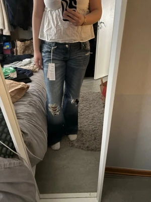 Blå loose jeans - Säljer ett par blå loose jeans med slitningar och hål på båda knäna. Jeansen har en klassisk femficksmodell, låg midja och är tillverkade i denim med tvättad effekt. Perfekta för en avslappnad och trendig look.