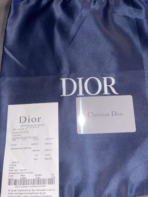 Svarta Dior sneakers med vita detaljer - Snygga svarta Dior sneakers med vita och grå detaljer. Skorna har en chunky sula, meshpaneler och reflekterande inslag. Klassisk snörning och Dior-logga på plösen. Perfekta för dig som vill ha en exklusiv och trendig look.