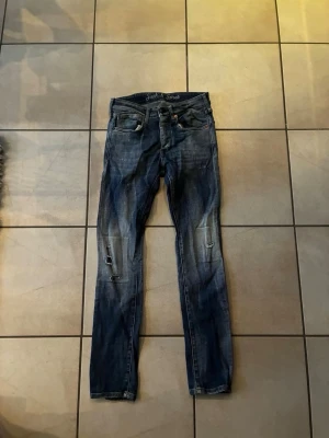 Mörkblå slitna jeans från Jack & Jones - Säljer ett par mörkblå jeans från Jack & Jones med skinny fit och slitningar på benen. Jeansen har klassisk femficksdesign, låg midja och detaljerade slitningar för en trendig look. Perfekta för dig som gillar en avslappnad och cool stil. W28 L 30 sitter väldigt bra köpta för 899 de är bara att höra av sig om de skulle vara nått