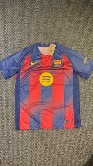 Barcelona matchtröja Nike röd/blå - Säljer en FC Barcelona matchtröja från Nike i röd och blå med gula detaljer. Tröjan har klubbmärke, Nike-logga och Spotify som sponsor framtill samt UNHCR-logga bak, perfekt för fotboll eller träning.