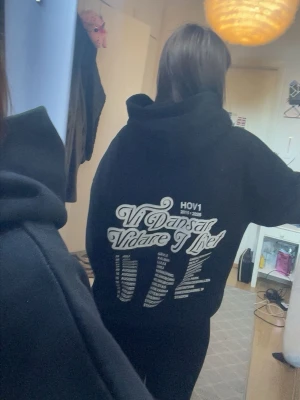 Hov1 hoddie ”vi dansar vidare i livet” pris kan diskuteras  - Pris kan diskuteras. Säljer en svart hoodie med en vit broderad krona på bröstet. Hoodien har en klassisk känguruficka framtill och huva med dragsko. Tillverkad i mjukt bomullsmaterial som är skönt att bära. Enkel och stilren design som passar till det mesta.