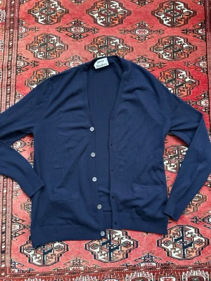 Acne Studios kofta - Stilren mörkblå cardigan från Acne Studios med knäppning framtill och två fickor. Tunn och mjuk kvalitet, perfekt för lager på lager. Klassisk design med långa ärmar och ribbade muddar. Passar till många olika looks.