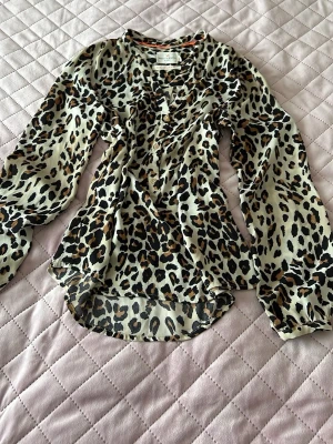 Leopardmönstrad blus med v-ringning - Snygg leopardmönstrad blus från H&M med v-ringning och transparent, luftig känsla. Blusen har långa ärmar med resår vid handlederna och rundad nederkant. Perfekt för dig som vill sticka ut med ett djurmönster.