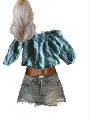 Ljusblå offshoulder blus med volang - Trendig ljusblå blus med offshoulder-design och volangdetalj längs halsringningen. Tillverkad i ett lätt, krinklat material och har långa puffärmar med resår vid ärmslut. Passar allt ifrån strl S-L 