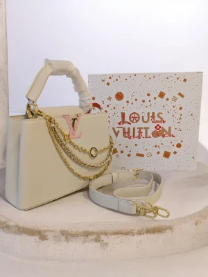 Iouis vuitton Capucines 🤍 - Den här specifika modellen har några utmärkende egenskaper: Design: Den har en sofistikerad benvit färg (off-white) med Iv-logotypen i en ljusrosa ton. Kedja: Den är utrustad med en dekorativ guldkedja i flera lager (multistrand). Modell: Denna storlek kallas vanligtvis Capucines BB eller Capucines MM, vilket är en av Iouis vuittons mest exklusiva och klassiska väskmodeller.