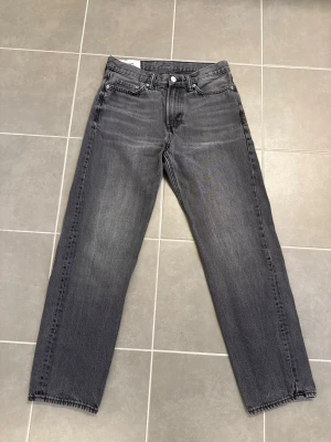 Grå raka jeans från HM, stl 32 - Säljer ett par grå jeans från Weekday med rak passform och klassisk femficksdesign. Jeansen har normal midja, knappgylf och är tillverkade i denim. Perfekta för en avslappnad och trendig look.