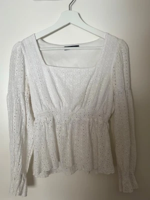 Vit spetsblus från SHEIN - Söt vit blus från SHEIN med broderade hålmönster och smock i midjan. Blusen har lång ärm, fyrkantig ringning och volangkant nedtill. Perfekt för en fräsch och romantisk look.