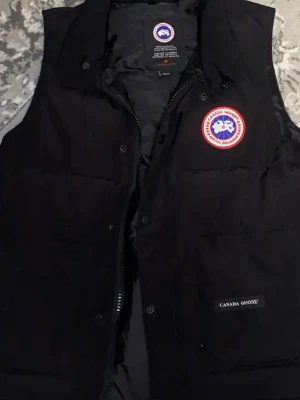 Svart dunväst från Canada Goose - Säljer en svart dunväst från Canada Goose med klassisk quiltad design. Västen är tillverkad i Kanada och har ett stilrent utseende utan synliga fickor eller detaljer på baksidan. Perfekt för lager-på-lager och håller dig varm under kyliga dagar.