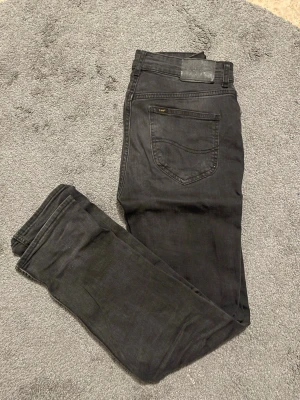 Svarta jeans från Lee - Snygga svarta jeans från Lee med klassisk femficksdesign och raka ben. Jeansen har en diskret Lee-logga på bakfickan och är tillverkade i ett mjukt denimtyg som ger en skön passform. Perfekta för dig som gillar en stilren och enkel look. Är i barnstorlek 14-15 år men sitter som 29-30 i midjan och 30 i längd ungefär. 