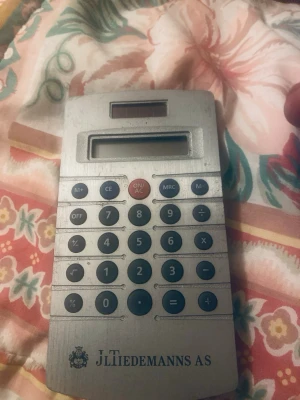 Metallisk miniräknare JL Tiedemanns - Snygg och stilren miniräknare i metall-look från JL Tiedemanns AS. Den har solcellspanel, svart display och svarta samt röda knappar. Perfekt för snabba uträkningar och enkel att ta med sig tack vare sin smidiga form.