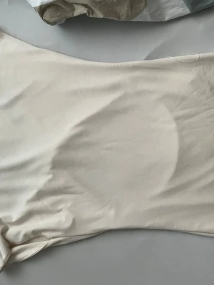 Vit omlott tubtopp med cut-out - Trendig vit tubtopp med omlottdetalj och stor cut-out framtill. Tunn, stretchig och mjuk i materialet med smala axelband.  Helt oanvänd