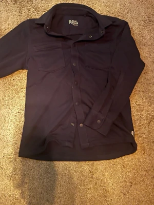 Mörkblå skjorta från Blue Ridge - Stilren mörkblå skjorta från Blue Ridge med klassisk krage och tryckknappar framtill. Skjortan har två bröstfickor och är långärmad, perfekt för en avslappnad men snygg look.