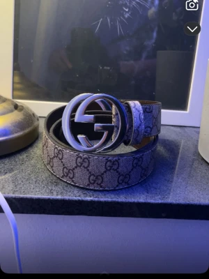 Gucci GG Supreme bälte med silverdetalj - Säljer ett klassiskt Gucci GG Supreme bälte med ikoniskt GG-mönster och stor silverfärgad logospänne. Bältet är i beige och brunt med tydliga GG-detaljer och passar perfekt till att lyfta vilken outfit som helst.