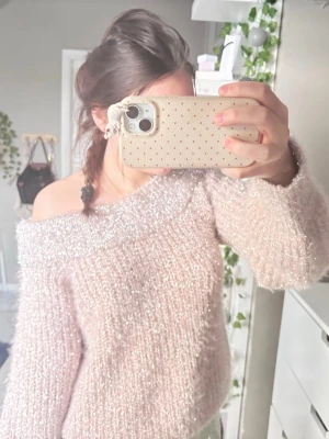 Glittrig off-shoulder stickad tröja - Superfin ljusrosa stickad tröja med glittriga trådar och off-shoulder design. Tröjan har lång ärm och en fluffig, mjuk känsla som ger en trendig look. Perfekt för dig som gillar att sticka ut med lite extra glitter.