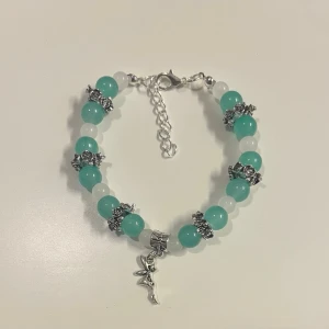  pärlarmband med tingeling berlock  - HANDGJORT armband med turkosa och vita pärlor, dekorerat med silvriga detaljer med en tingeling berlock. Armbandet har justerbar kedja och karbinlås för enkel användning. 