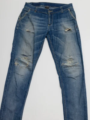 Blå slitna jeans från Dondup  - Säljer ett par blå dondup jeans med slitningar och hål på både fram- och baksida. Jeansen har klassisk femficksmodell, normal midja och raka ben. Materialet är denim i bomull och de har en snygg tvättad look med ljusa partier.
