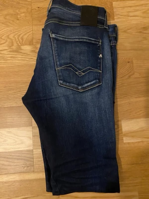 Mörkblå jeans från Replay - Snygga mörkblå jeans från Replay med klassisk femficksmodell och diskreta slitningar framtill. Jeansen har raka ben och kontrastsömmar samt en unik detalj på bakfickan. Perfekta för en avslappnad och trendig stil och priset kan diskuteras 
