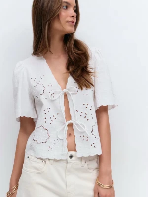 Vit broderad blus med knyt - Superfin vit blus med broderade detaljer och hålmönster. Toppen har korta ärmar, v-ringning och två knyt framtill. Den är croppad med vågig kant nertill och är perfekt för varma dagar.