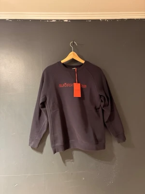 Svart sweatshirt från Björn Borg - En stilren svart sweatshirt från Björn Borg med röd logotyp broderad på bröstet. Tröjan har rund halsringning, långa ärmar och ribbade muddar vid ärmslut och nederkant. Perfekt för en avslappnad och sportig look.