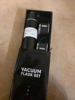 Svart vakuumflaska set 500ml - Snyggt vakuumflaska set i svart med en termos på 500ml och två matchande muggar. Perfekt för att ta med varm eller kall dryck. Flaskan och muggarna har en stilren design i metall och plast. Levereras i originalförpackning.