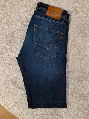 Mörkblå jeans från Replay GROVER - Snygga mörkblå GROVER jeans från Replay med klassisk femficksmodell och kontrastsömmar. Jeansen har en läderpatch med Replay-logga bak i midjan och diskreta röda detaljer vid bakfickan. Tillverkade i slitstarkt denimtyg som ger en tidlös look.