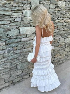 Vit långklänning med volanger - Säljer en vit långklänning med tunna axelband och flera lager volanger. Klänningen har öppen rygg och en romantisk, flowy siluett som passar perfekt till sommaren. Perfekt för dig som vill ha en elegant och luftig look.