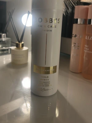 Bobbys Hair Care Torrschampo - Volymgivande torrschampo från Bobbys Hair Care Sweden. Kommer i en vit cylinderformad flaska med gulddetaljer och text. Vegansk formula och tillverkad i Sverige. Perfekt för att fräscha upp håret snabbt.