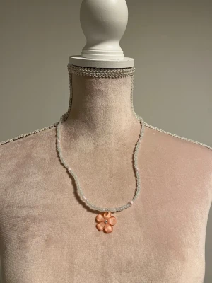 Halsband med pärlor och blomma (rosa) - NY! 🌺 Sött halsband med med små vita och ljusrosa pärlor samt ett hänge i form av en rosa blomma. Går att justera längden lite.  Köpt från en small business i USA (etsy). Säljer även den blåa versionen om man vill ha som bff halsband :3