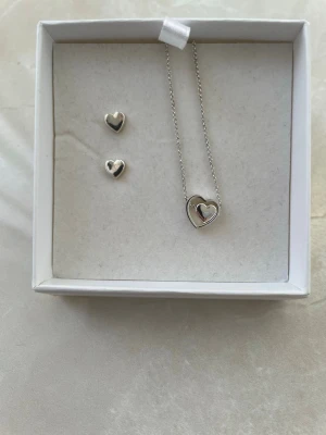 Smyckesset med hjärtan i silverfärg - Säljer ett smyckesset med halsband och örhängen i silverfärg. Halsbandet har ett hjärthänge och örhängena är små hjärtan. Perfekt för dig som gillar stilrena accessoarer med romantisk touch.