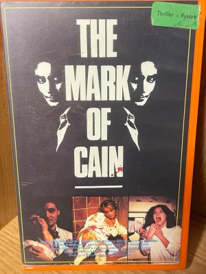 The Mark of Cain VHS thriller - Säljer en VHS-film med titeln 'The Mark of Cain'. Omslaget har en mörk design med vita bokstäver och bilder från filmen. Filmen är en thriller/rysare och utgiven av Prisma Film & Video. Text på svenska på baksidan.