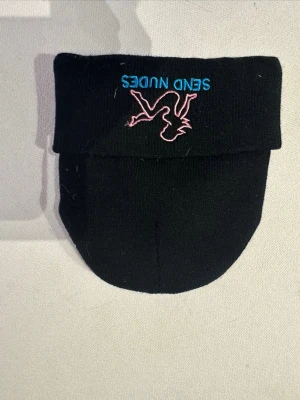 Svart mössa med broderi och text - Svart mössa i stickat material med vikt kant. På framsidan finns ett broderat motiv av en rosa siluett och blå texten 'SEND NUDES'. Perfekt accessoar för dig som vill sticka ut lite extra.