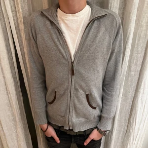Grå kofta från Massimo Dutti för 449kr - Säljer en stilren grå kofta från Massimo Dutti i mycket bra skick. Den har en dragkedja framtill och två fickor med bruna detaljer. Perfekt för höst och vår, och passar både till vardags och lite finare tillfällen. Storleken är som XS och passar någon runt 160-170, den har en normal passform.