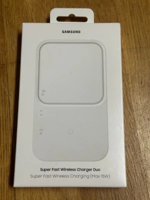 Samsung Super Fast Wireless Charger Duo - Trådlös laddare från Samsung med plats för två enheter samtidigt. Vit, rektangulär design med rundade hörn. Stödjer upp till 15W snabbladdning och fungerar med både mobil och Galaxy Watch eller Buds. Perfekt för dig som vill ladda flera prylar samtidigt utan sladdar.