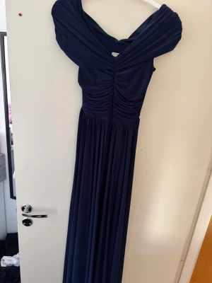 Marinblå balklänning offshoulder - Elegant marinblå långklänning med offshoulder-design och vackra draperingar över bysten från Bubbleroom 2025. Liten slits även vid kjolen. Bystens längd (från vecket) är 22cm och kjolens längd mätt från mitten av bystets undre veck är 116cm i längd. Personen på bilden är 174cm lång och hade ballerinaskor utan klack! Så är definitivt lång men kan definitivt sys upp av er själva efter längd. Användes bara en gång i ca 4 timmar på finsittning och sedan helt oanvänd! 🥰