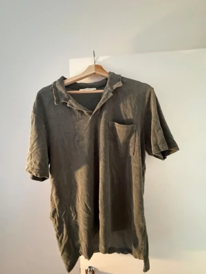 Olivgrön frotté piké från A Day's March - Säljer en olivgrön henley från A Day's March i mjuk bomull. Skjortan har korta ärmar, öppen krage och en bröstficka. Perfekt för dig som gillar en avslappnad och stilren look.